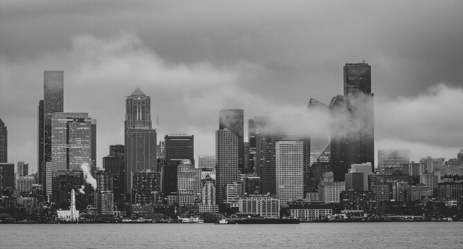 Seattle skyline form West Seattle across Elliott Bay on a rainy afternoon with wisps of low clouds and fog drifting through the tall buildings; Seattle, Washington, United States of America