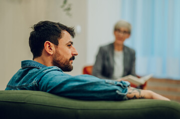 A young man with problems is sitting on a sofa during a session with a psychotherapist.
