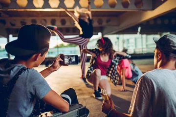 Fotobehang Young and diverse group of people breakdancing and filming it on a smartphone in a parking lot © Geber86