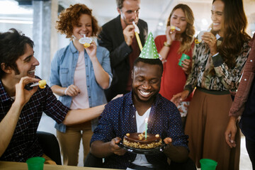 Young and diverse group of people celebrating a surprise birthday party in the office of a startup...