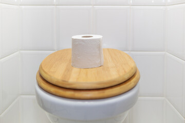 body, bathroom and personal hygiene, a closed wooden toilet lid with a full new roll of toilet paper