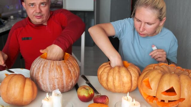 Young family two people carving pumpkins to make Jack O Lanterns for Halloween eve. Removing the pulp with your hands from pumpkins. Decoration celebrating holiday saints night.