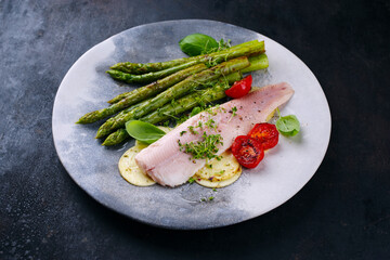 Grüner glasierter Spargel mit geräuchertes Regenbogenforellen Filet, Croxetti Pasta und Cherry Tomaten serviert als close-up auf einem Design Teller mit Textfreiraum