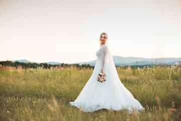 a shot of a beautiful bride in a white lace dress holding a bouquet of dried flowers in the middle...