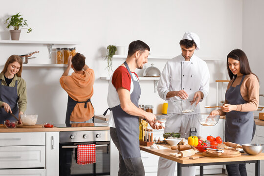 Group of young people with Italian chef preparing pizza during cooking class in kitchen