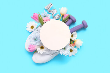 Blank card with sneakers, dumbbells, tape measure and spring flowers on blue background
