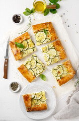 Healthy baked zucchini galette tart cutted into pieces on light table, top view