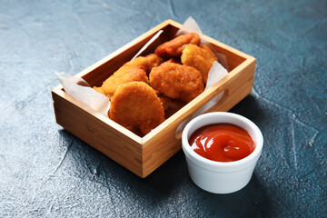 Wooden box with delicious nuggets and bowl of ketchup on dark blue table