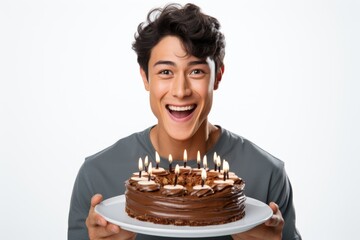 A young man is holding a chocolate cake with lit candles. This image can be used for birthday celebrations or special occasions.