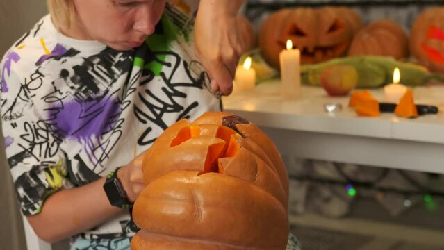 Focused woman carving knife halloween Jack O Lantern pumpkin at home for party decoration, flickering candles in the background. Preparing pumpkin for happy holiday Halloween. Close up.