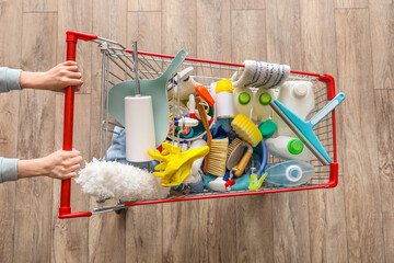 Woman with shopping cart full of cleaning supplies on wooden floor, top view