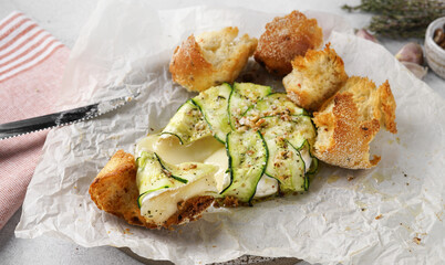 Baked Brie camembert cheese with zucchini with nuts, herbs and olive oil. Served with wine and bread