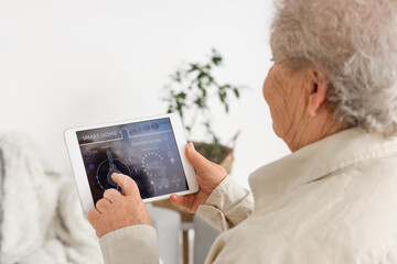 Senior woman using smart home security system control panel, closeup