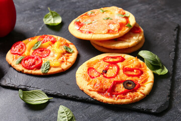 Board with different tasty mini pizzas on black background