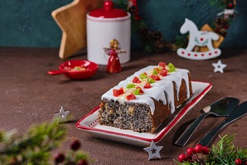Dessert, Polish poppy seed cake with apples and candied fruits, covered with sugar icing, in Christmas style on a brown concrete background. Merry Christmas. Polish cuisine