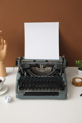 Vintage typewriter with cup of coffee, wooden hand and candle on white table near brown wall