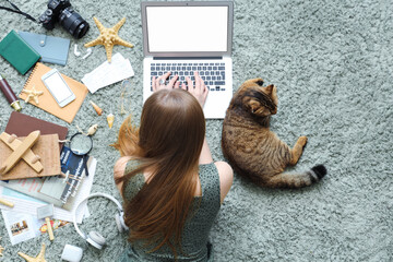Woman with Scottish fold cat and travelling accessories using laptop on green carpet, top view