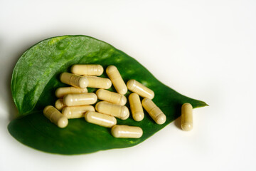 Vitamin D capsules on a green leaf with white background.