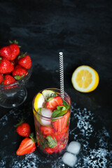 Glass of fresh mojito and bowl with strawberry on grunge black background