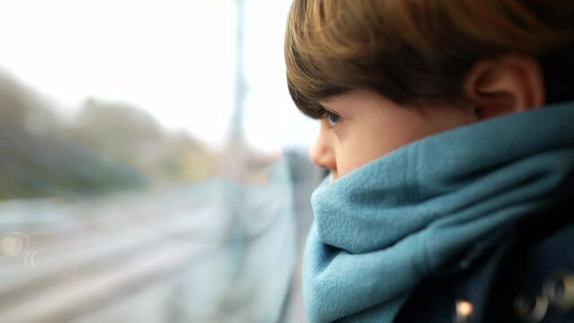 Little boy leaning on train window looking at landscape pass by at high-speed. Child wearing scarf staring at view in motion