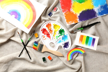 Artist's palette and brushes with paints and drawings on cloth background