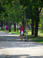 a beautiful girl walks along a path in the park and rolls a bicycle next to her. athlete resting after training. nature walks and active lifestyle