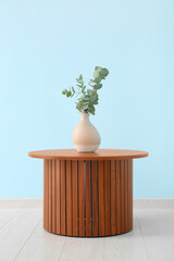 Wooden coffee table with eucalyptus branches in vase near blue wall