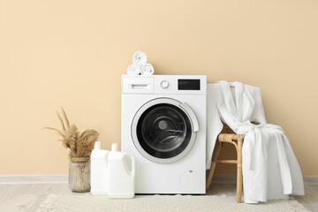 Washing machine, stool with bathrobe and bottles of detergent near beige wall