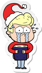 hand drawn sticker cartoon of a crying man holding book wearing santa hat