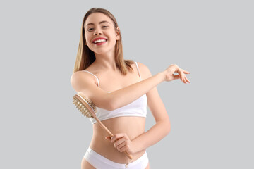 Young woman massaging her arm with anti-cellulite brush on light background