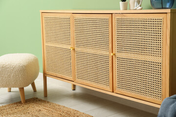 Chest of drawers with floor mat and pouf near green wall