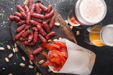pieces of cured meat carpaccio, Mini Sausages, Smoked Salami Sticks, Cabanossi, Kabanos, wooden cutting board, glasses with beer, on a black isolated background