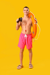 Male lifeguard with binoculars and ring buoy on yellow background