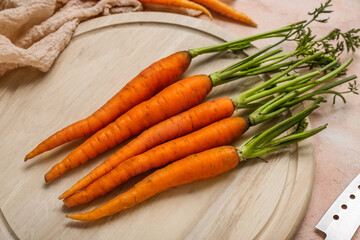 Tasty fresh carrots and wooden board on orange textured background