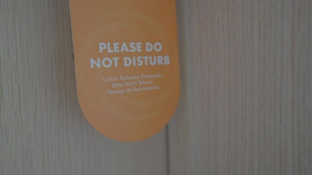 Do Not Disturb orange tag sign hanging on door handle. Visitors warning hotel staff with orange sign to take some rest in room