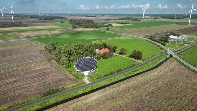 Aerial footage from solar panels on the roof of the farm barn with power line, electricity relay station and wind turbines on the background. Barn roof solar panels and renewable energy landscape.
