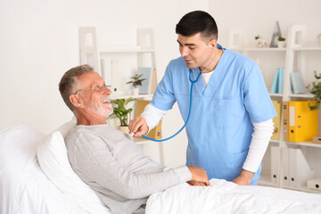 Obraz premium Male nurse hearing senior man with stethoscope in bedroom