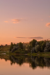 Fototapeta na wymiar Lake during a calm, reflecting hills, fields, and trees, against a backdrop of orange sunset sky.