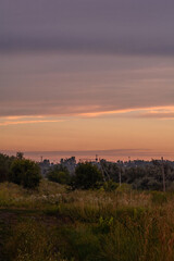 Obraz premium Green fields with electric poles on them, against a sunset sky with clouds, during the golden hour.