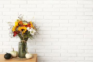 Wooden cabinet with bouquet of autumn flowers and pumpkins near white brick wall