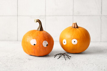 Funny pumpkins with drawn eyes and spiders on white grunge table