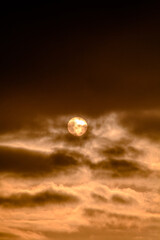 Yellow sun disk hidden behind dark clouds, illuminated by this sun