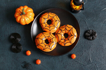 Plate of tasty donuts with decorations for Halloween on black background