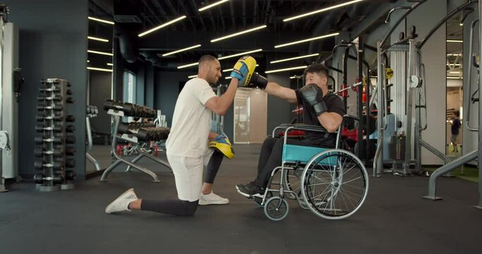Disabled athlete in wheelchair works out punches with a coach