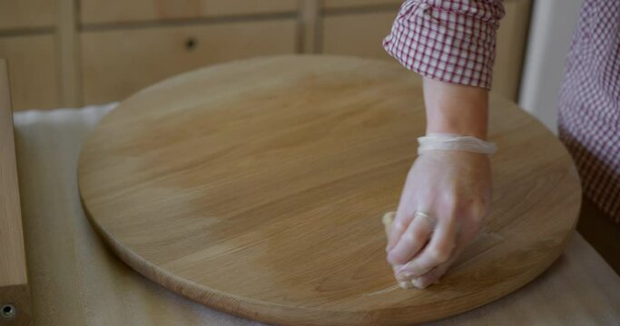 A close-up of a carpenter's male hand in a silicone glove processes the tabletop of a tea table with oil for wood. Application of a protective coating on a joiner's product. High quality 4k footage