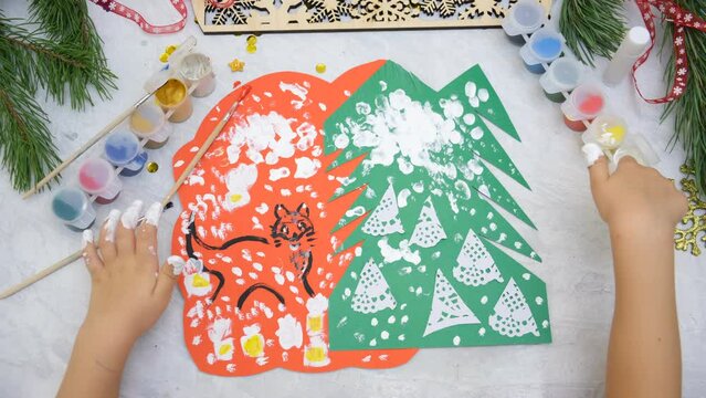 Child making a greeting card, Craft for children. Nice greeting card with a Christmas snowy forest. Top view, finger painting