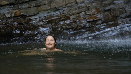 Young woman bathing in a small lake within the mountain. Creative. woman swimming under the falling drops of waterfall water.