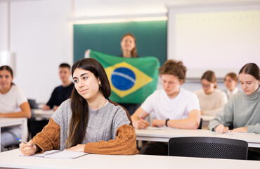 Students study in classroom, teacher stands behind with flag of Brazil