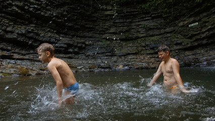 Young boys bathing in a small lake within the mountain. Creative. Little boys splashing cold water.