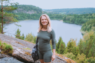 Blonde woman in her 50s walking on rocks above a lake